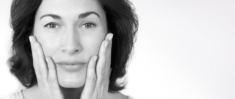 Mujer de mediana edad tocándose las mejillas con ambas manos.