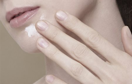 Mujer aplicándose crema en la barbilla.