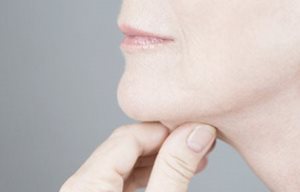 Mujer estirando la piel de su mentón con la mano.