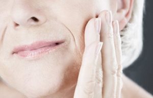 Mujer mayor tocándose la mejilla izquierda con la mano