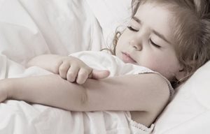 Niña pequeña rascándose el brazo.